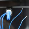 Detailaufnahme von blauen Kabeln und einem Anschluss für die mobile Wasserversorgung, ideal für Campingbedarf und den Umbau von Transportern. Diese Produkte unterstützen die Installation von Waschbecken und Pumpen in Fahrzeugen und Marktständen.