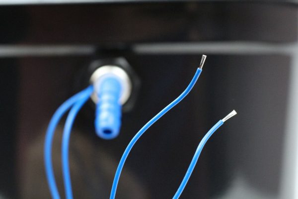 Detailaufnahme von blauen Kabeln und einem Anschluss für die mobile Wasserversorgung, ideal für Campingbedarf und den Umbau von Transportern. Diese Produkte unterstützen die Installation von Waschbecken und Pumpen in Fahrzeugen und Marktständen.