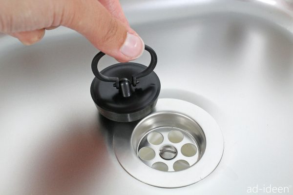 Hand, die einen Deckel für den Abfluss eines Edelstahlwaschbeckens anhebt, ideal für mobile Wasserversorgungslösungen beim Camping oder für Marktstände.